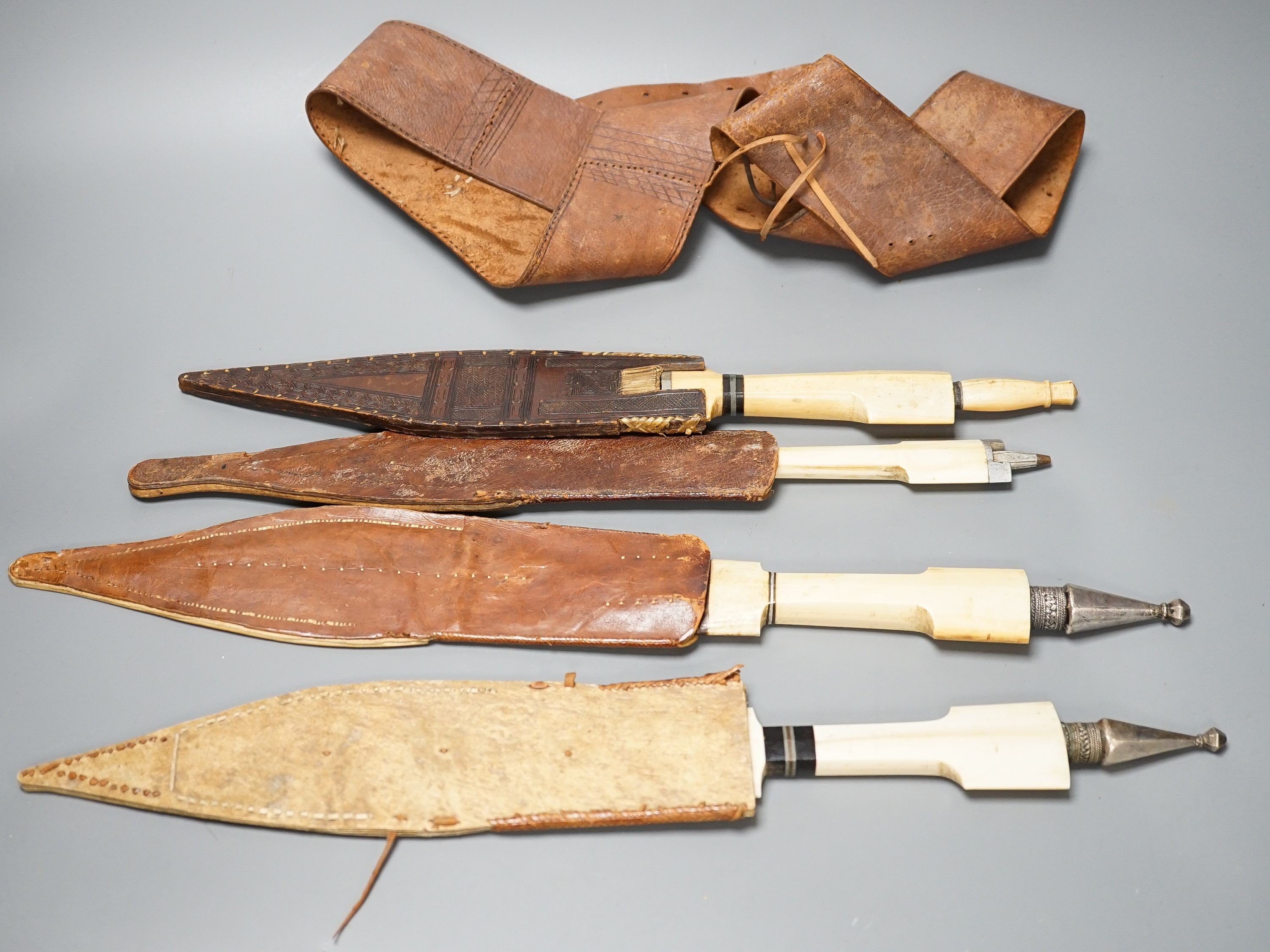 Four similar African tribal daggers c.1900, each with hippo tusk handle including two with silver pommels, all in their decorated leather scabbards with 1 belt, maximum 45cms.